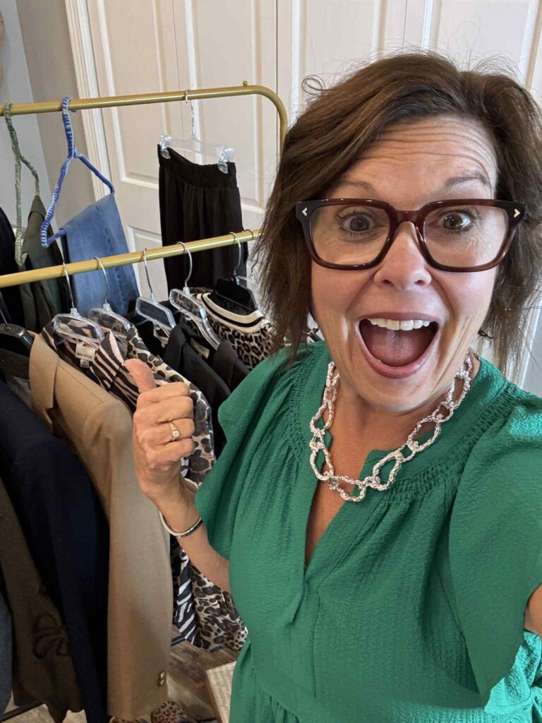 Woman smiling and giving a thumbs up in front of a clothing rack, celebrating a simplified capsule wardrobe closet.