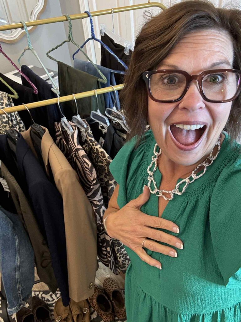 Woman in green dress looking delighted in front of a clothing rack, reacting with excitement to her capsule wardrobe.