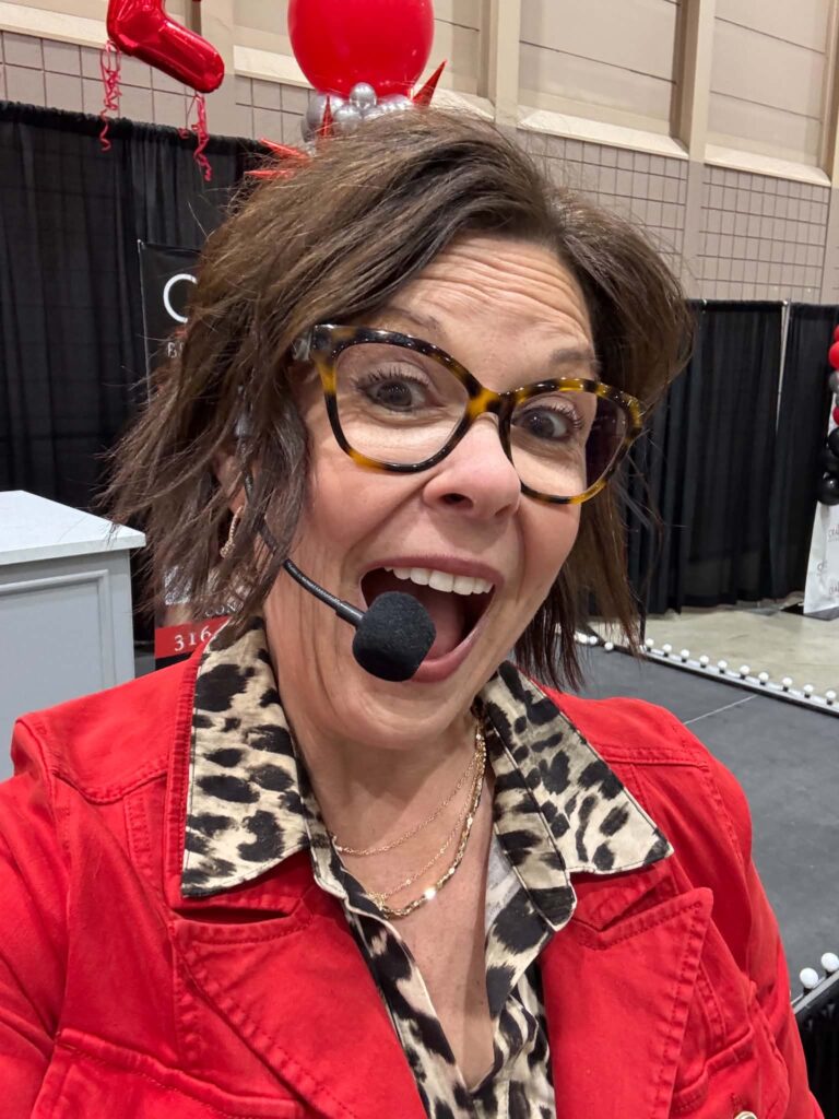 Royanna Stratmoen of Radiate with Royanna speaking on stage at The Women's Fair in Wichita, Kansas wearing a red blazer and headset microphone